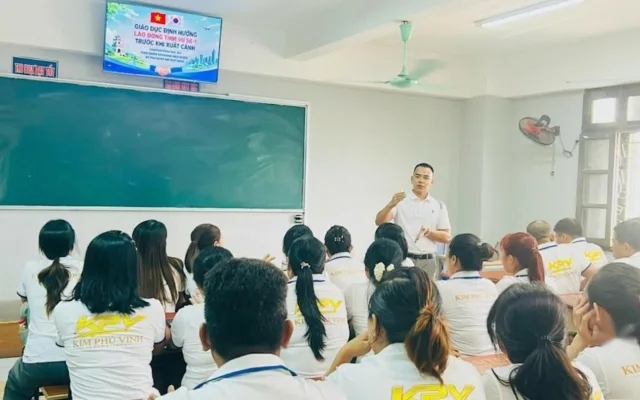 Người đứng giảng cạnh bảng xanh, học viên áo đồng phục trắng ngồi nghe trong lớp – lớp học tiếng Nhật tại KPV Đồng Nai