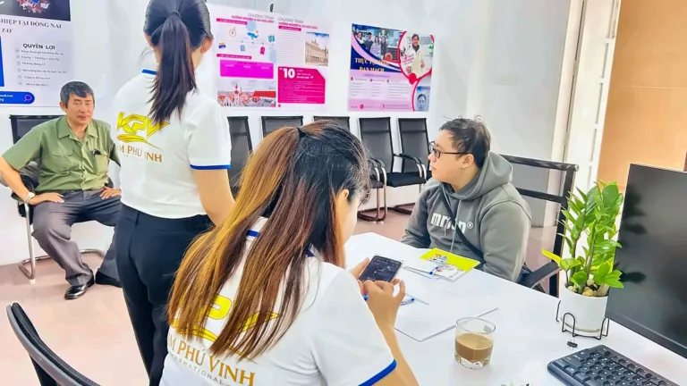 Hai nhân viên áo KPV tiếp một khách tại bàn, sau lưng là poster du học Đức – việc làm trong nước, doanh nghiệp FDI