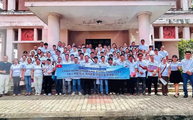 Ảnh tập thể đoàn đông người dưới hiên tòa nhà, cầm băng rôn chào mừng đoàn E8-1