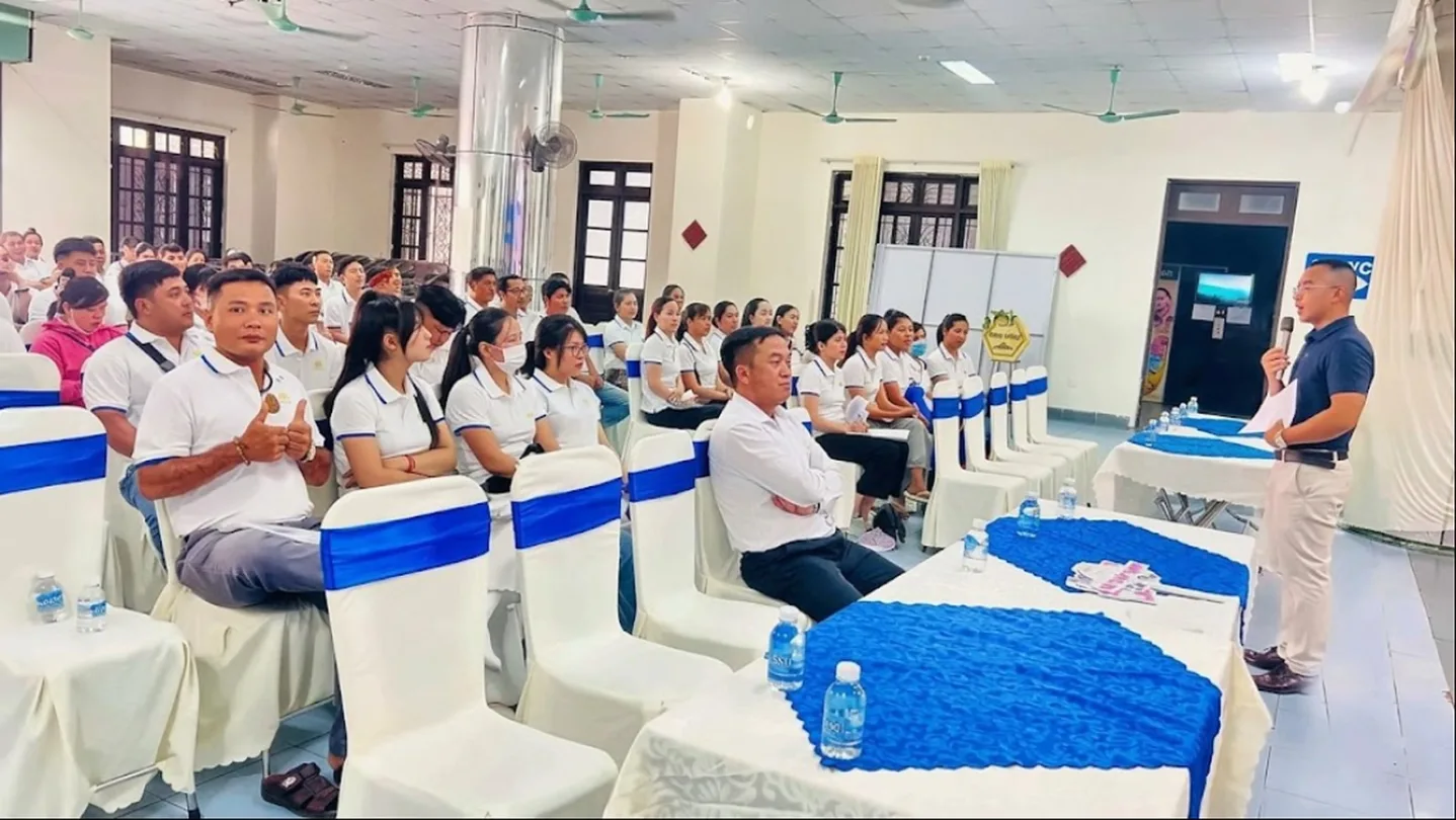 Người cầm micro phát biểu trước hội trường đông người, ghế thắt nơ xanh – workshop hướng nghiệp tại trường cùng KPV