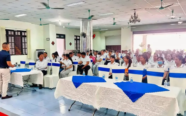 Hội trường đông người áo trắng nghe người cầm micro đứng cạnh bàn khăn xanh – hoạt động định hướng, tư vấn tại KPV